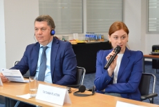 dwoje uczestników siedzą przy stole, pani mówi przez mikrofon