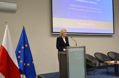 Przy mównicy stoi kobieta i przemawia.